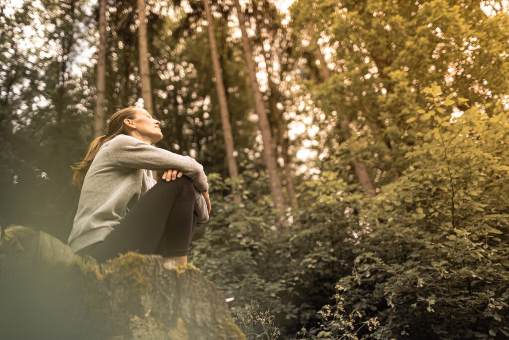 person sitting in nature looking up at trees